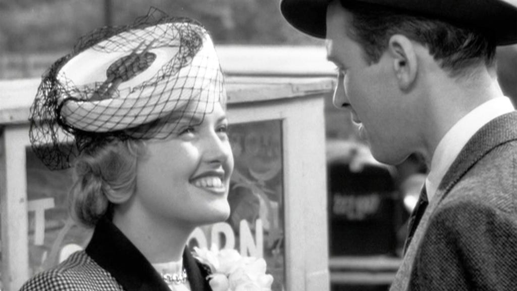 Virginia Patton in 'It's a Wonderful Life' smiling at her on-screen brother-in-law, played by James Stewart. She wears a fascinator hat and floral pin on her shoulder.