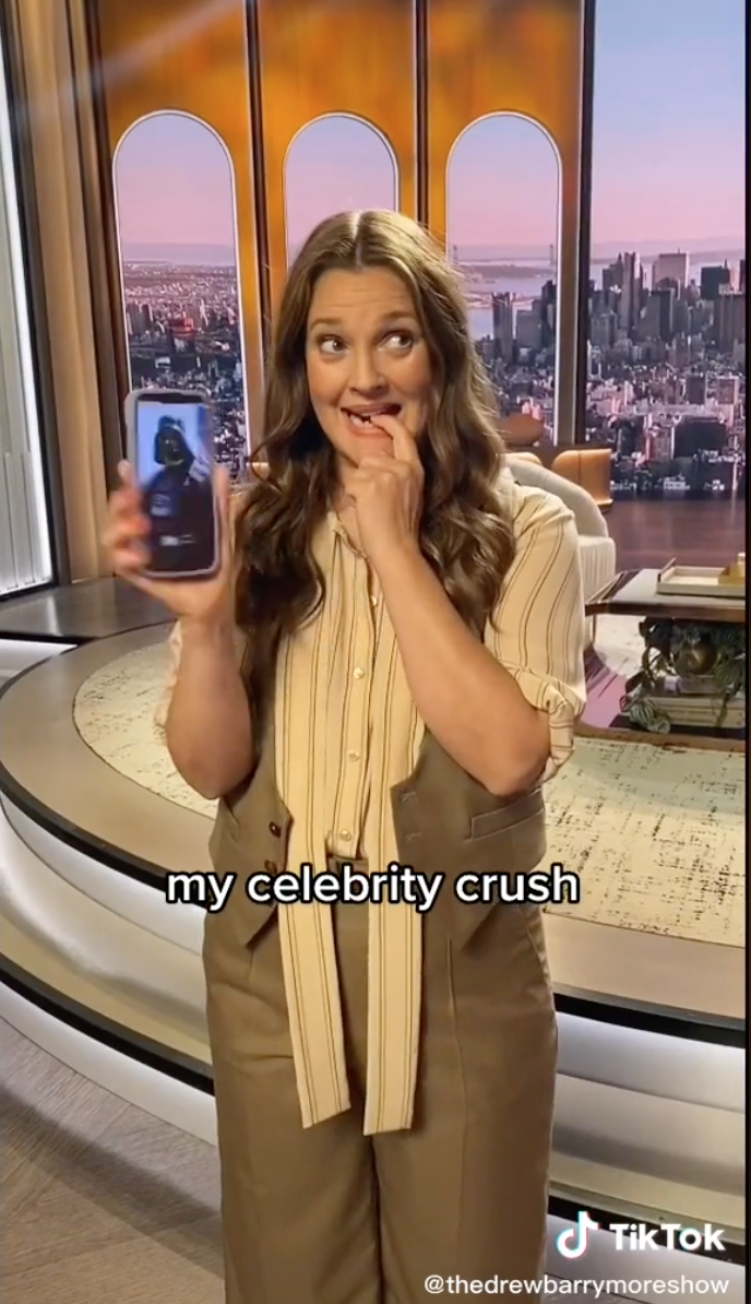 Drew Barrymore on set of Drew Barrymore show wearing a cream blouse. The caption reads "my celebrity crush" and she had her finger in between her teeth.